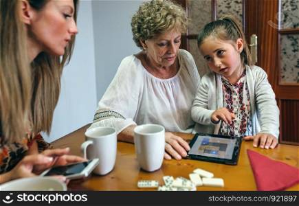 Little girl asking permission to her mother to continue playing the tablet with her grandmother. Little girl asking permission to continue playing tablet