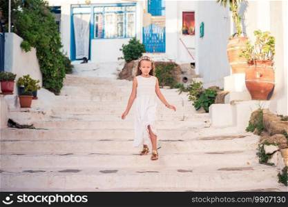 Little girl at street of typical greek traditional village with white walls and colorful doors on Mykonos Island, in Greece. Kid at street of typical greek traditional village with white walls and colorful doors on Mykonos Island