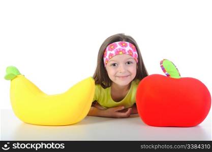 little girl at the table with a big banana and apple. Isolated on white background