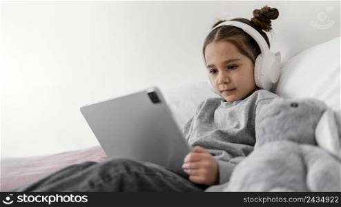 little girl bed with headphones using tablet 2