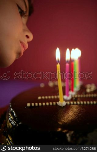 Little girl blowing birthday chocolate cake candles in a row over red background