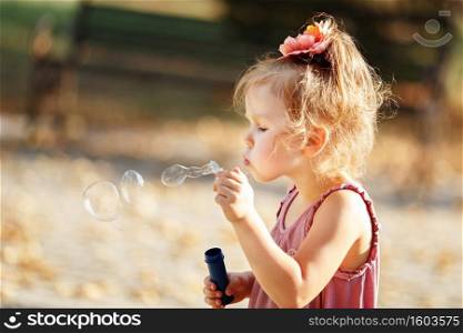 little girl blowing soap bubbles in autumn park