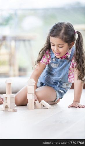 Little girl building blocks while sitting on hardwood floor