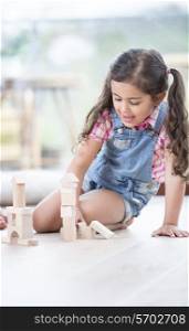 Little girl building blocks while sitting on hardwood floor