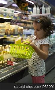 Little girl buying cheese in supermarket. Child hold small basket in supermarket and select cheese from store showcase. Concept for children selecting products in shop.