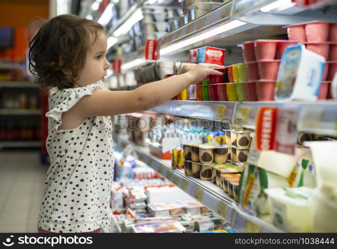 Little girl buying yogurt in supermarket. Child in supermarket select products from store showcase. Concept for children selecting milk products in shop.