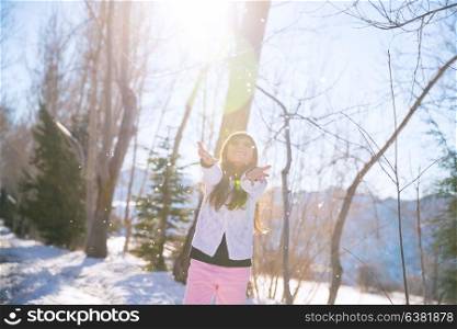 Little girl catching snowflakes in winter park, happy active child, having fun outdoors in bright sunny day, enjoying winter holidays, playing games outdoor