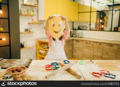 Little girl chef made a funny face out of dough, cookies preparation on the kitchen, funny baker. Kids cooking pastry, child cook, children preparing cake. Little girl chef made a funny face out of dough