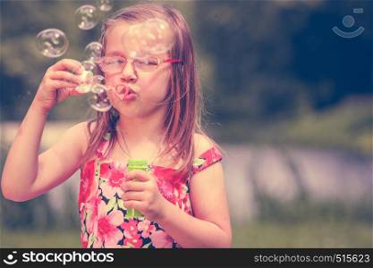Little girl child blowing soap bubbles outdoor. Kid having fun in park. Happy and carefree childhood. Instagram filtered.. Little girl child blowing soap bubbles outdoor.