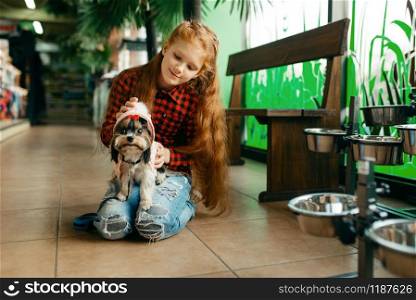 Little girl choosing clothes for her dog in pet store. Child buying equipment in petshop, accessories for domestic animals. Little girl choosing clothes for dog in pet store