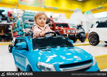 Little girl choosing electromobile in kids store, front view. Daughter buying toys in supermarket, family shopping, young customer