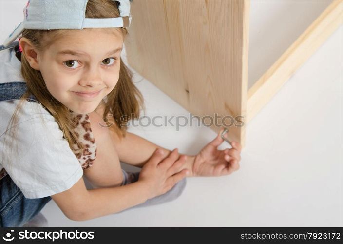 Little girl - collector of furniture twists the screw on the dresser. Girl in overalls collector furniture screw spins