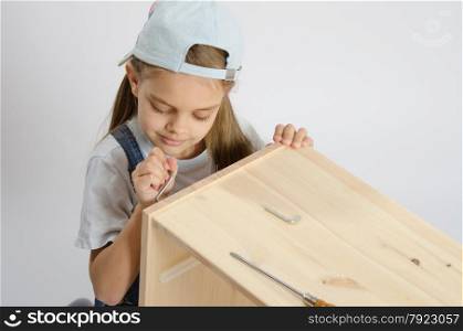 Little girl - collector of furniture twists the screw on the wooden frame of the chest. Little girl in the image of garbage furniture screw spins