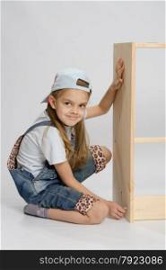 Little girl - collector of furniture twists the screw on the wooden frame of the chest. Little girl in overalls collector of furniture turn screw on dresser