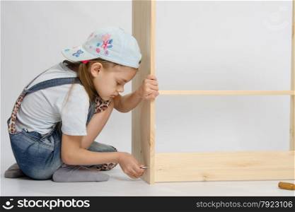 Little girl - collector of furniture twists the screw on the wooden frame of the chest. Little girl in overalls collector furniture screw spins