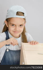 Little girl - collector of furniture with a hex wrench around a wooden frame chest. Girl clothing collector furniture screw screw-Allen