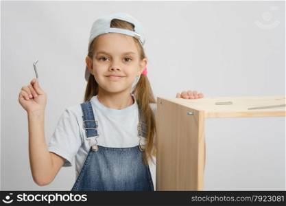 Little girl - collector of furniture with a hex wrench around a wooden frame chest. Little girl in image collector of furniture with tools