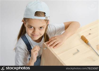 Little girl - collector of furniture with a hex wrench around a wooden frame chest. Little girl in dress collector furniture screw screwed Allen