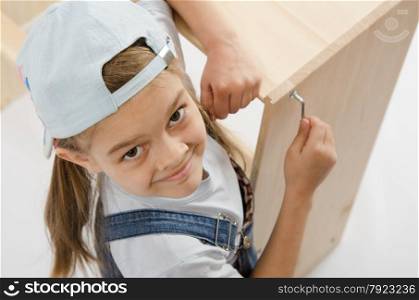 Little girl - collector of furniture with a hex wrench around a wooden frame chest. Little girl in dress collector furniture tighten screws Allen