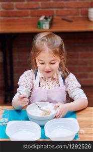 Little girl combining the ingredients for baking the cake. Kid taking part in baking workshop. Baking classes for children, aspiring little chefs. Learning to cook. Combining and stirring prepared ingredients. Real people, authentic situations