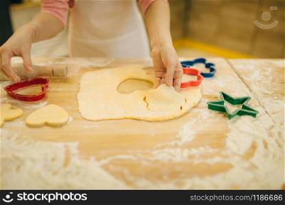 Little girl cook in apron makes cookies in the shape of a heart on the kitchen. Kid cooking pastry, child chef preparing cake. Little girl makes cookies in the shape of a heart