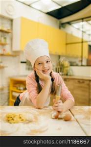Little girl cook in cap and apron holds whisk for mixing, cookies preparation on the kitchen. Kids cooking pastry, children chefs preparing cake
