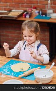Little girl cutting the dough to heart shapes cookies. Kid taking part in baking workshop. Baking classes for children, aspiring little chefs. Learning to cook. Combining and stirring prepared ingredients. Real people, authentic situations