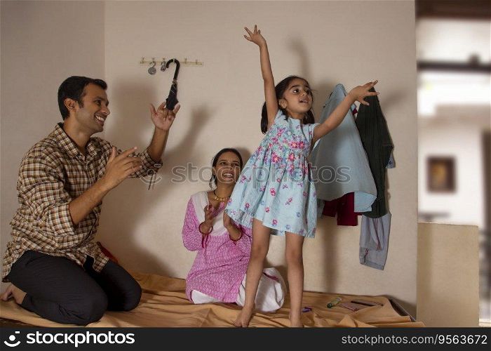 Little girl dancing on bed while her parent sitting behind