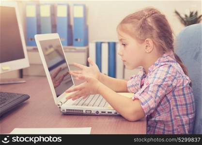 Little girl doing homework on the laptop, education at home, emotionally with gesturing resolving difficult task, modern educational process of a little kids