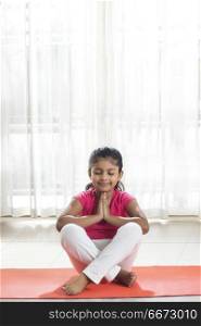 Little girl doing prayer on yoga mat at home