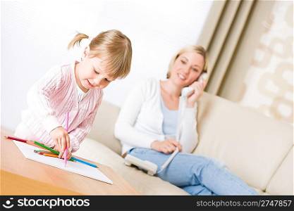 Little girl draw with color pencil in lounge, mother with phone calling in background