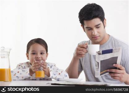 Little girl drinking juice while father reading newspaper
