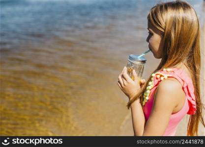 little girl drinking juice while standing beach