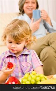 Little girl eat strawberry fruit with grandmother relaxing on sofa