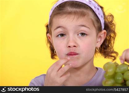 Little girl eating bunch of green grapes