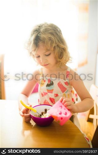Little girl eating corn balls in the kitchen. Morning light