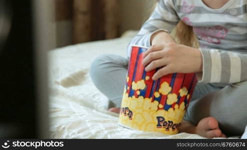 Little girl eating popcorn and watching TV at home