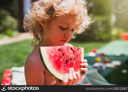 Little girl eating watermelon on the grass in summertime