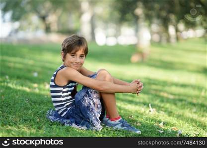 Little girl, eight years old, sitting on the grass in an urban park.. Little girl, eight years old, sitting on the grass outdoors.