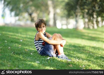Little girl, eight years old, sitting on the grass in an urban park.. Little girl, eight years old, sitting on the grass outdoors.