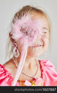 Little girl enjoying her role of princess. Adorable cute 5-6 years old girl wearing pink princess dress holding magic wand at front of her face standing on plain background. Little girl enjoying her role of princess. Adorable cute 5-6 years old girl wearing pink princess dress holding magic wand