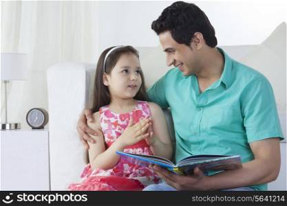 Little girl explaining story to father on sofa at home