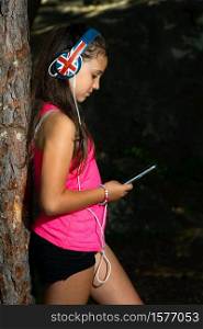 Little girl explores social networks with her smartphone while listening to music appeased to a plant.