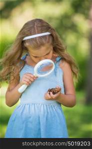 Little girl exploring the cone through the magnifying glass outdoors