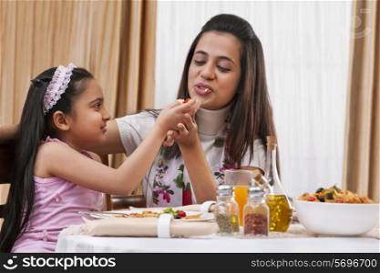 Little girl feeding her mother piece of pizza at restaurant