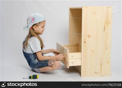 Little girl - furniture collector tries to insert a box in a wooden chest of drawers. Girl in overalls furniture collector tries to insert drawer a chest of drawers