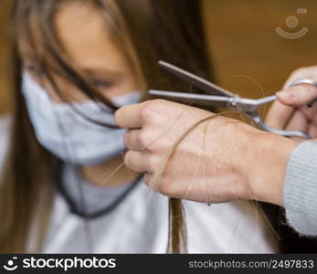 little girl getting haircut while wearing medical mask