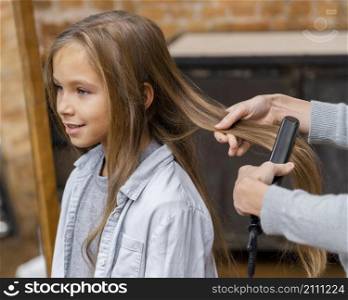 little girl getting her hair straightened by beautician