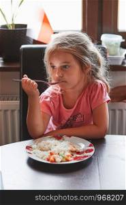 Little girl having a dinner at home. Meal on a plate on table, kid holding a fork. Real people, authentic situations