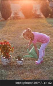 Little girl helping to water the flowers growing in flower pot, pouring water from green watering can, working in backyard at sunset. Candid people, real moments, authentic situations